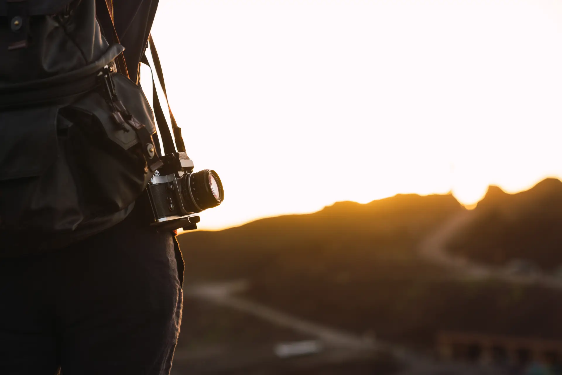 Back view of crop tourist with knapsack and retro camera standing on mountain Teide in evening on blurred background in Tenerife, Canary Islands, Spain