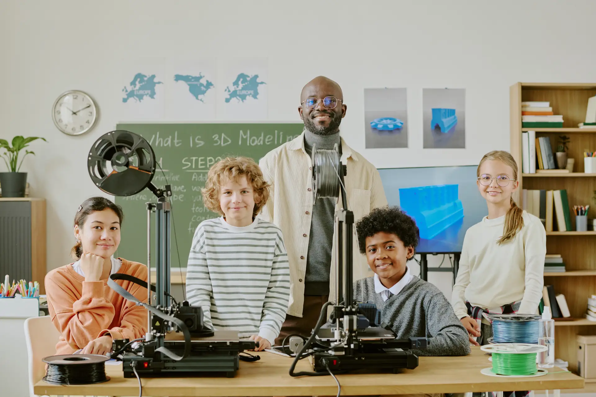 Multi-ethnic students learning 3D modeling with devices and technology in classroom setting. Teacher demonstrating a process while students actively engaging and participating in activities